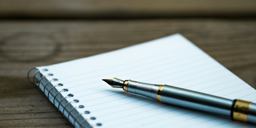 A view of a white spiral notebook on a table with a golden fountain pen kept on it.