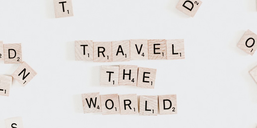White and black pieces of scrabble saying travel the world on a plain white background.