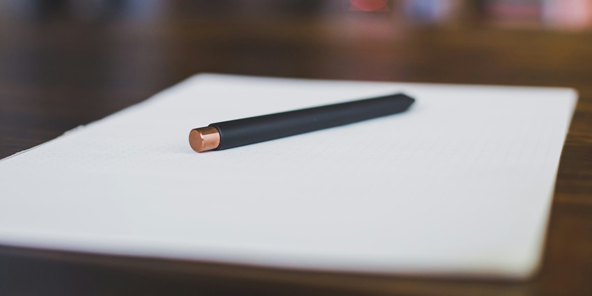 A view of a black pen kept on a white piece of paper on a table with a blurred background.