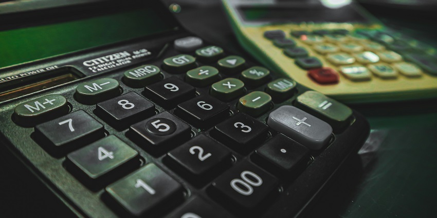 A focused view of two white and black calculators sitting on top of a brown table.