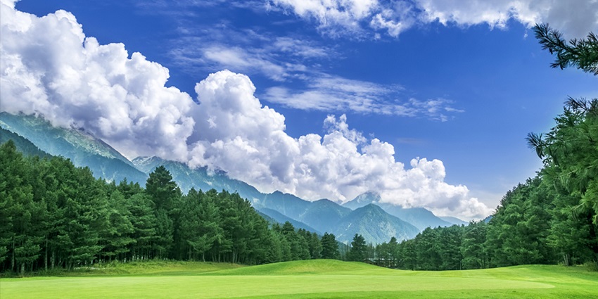 View of the golf course in Pahalgam surrounded by tall pine trees & snow-capped mountains