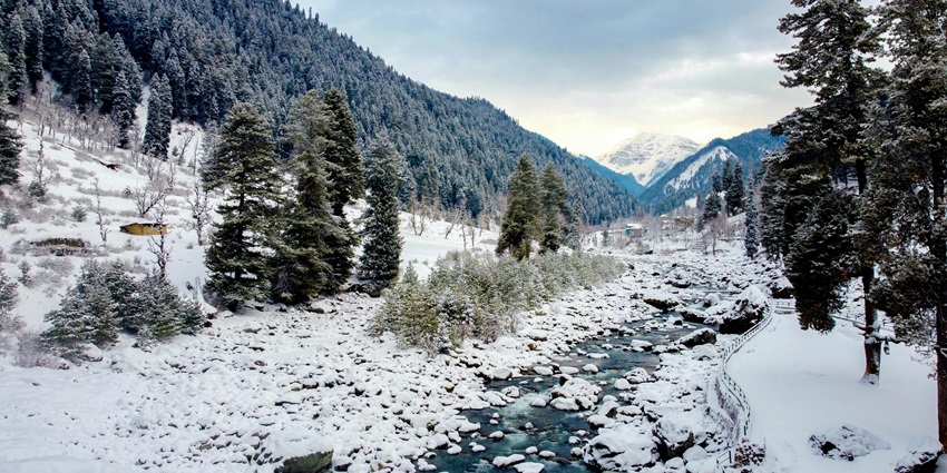 A breathtaking view of snow-covered Pahalgam and a stream of water flowing through.
