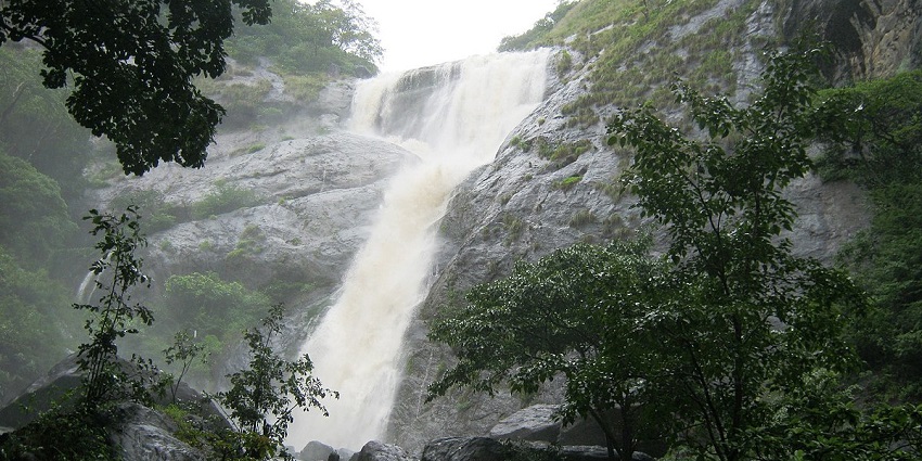 Waterfall cascading down rocks, surrounded by lush green forest - waterfalls in Kollam