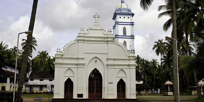 A frontal view of a historical church in Guruvayur with a white exterior, surrounded by trees