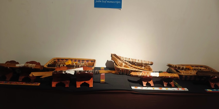 Picture of multiple palm-leaf manuscripts showcased in a museum with historical artefacts
