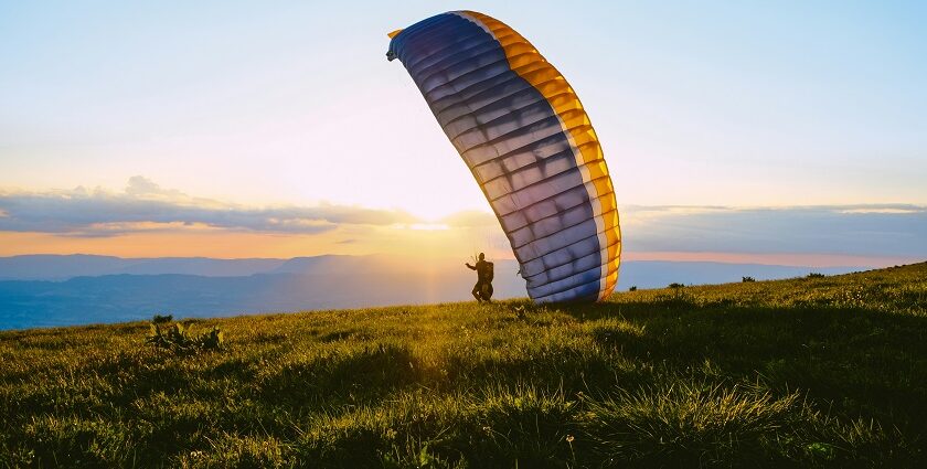 A silhouette of a person standing on lush green grass holding a paragliding parafoil.