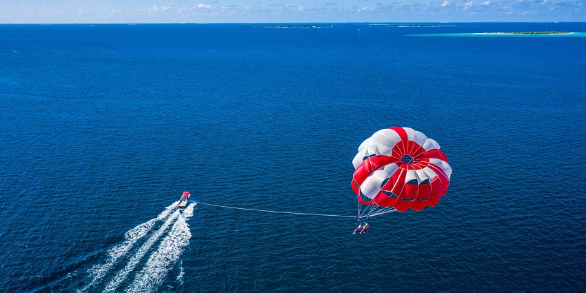 View of two tourists enjoying the thrill of parasailing with a boat over vast ocean waters