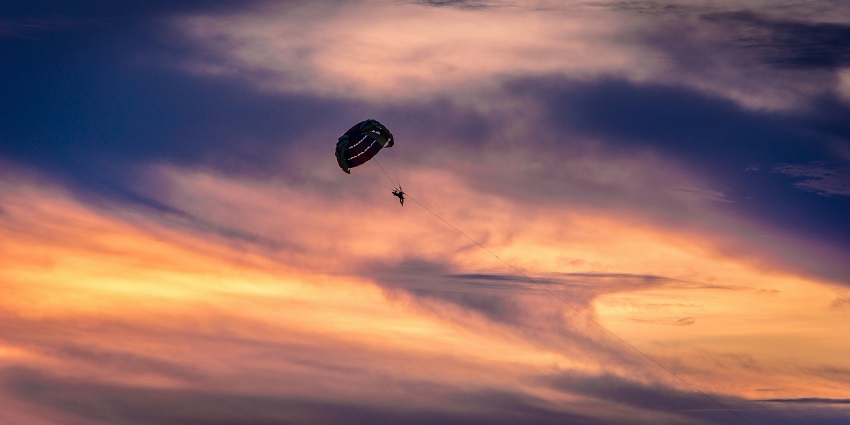 A breathtaking view of a person parasailing in the backdrop of a stunning purple sky.