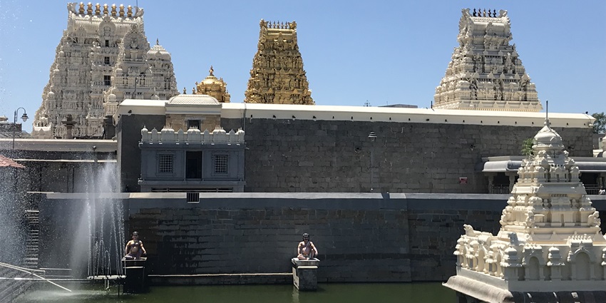 A scenic temple in Munnar with multiple marble shrines and a pond in front of it