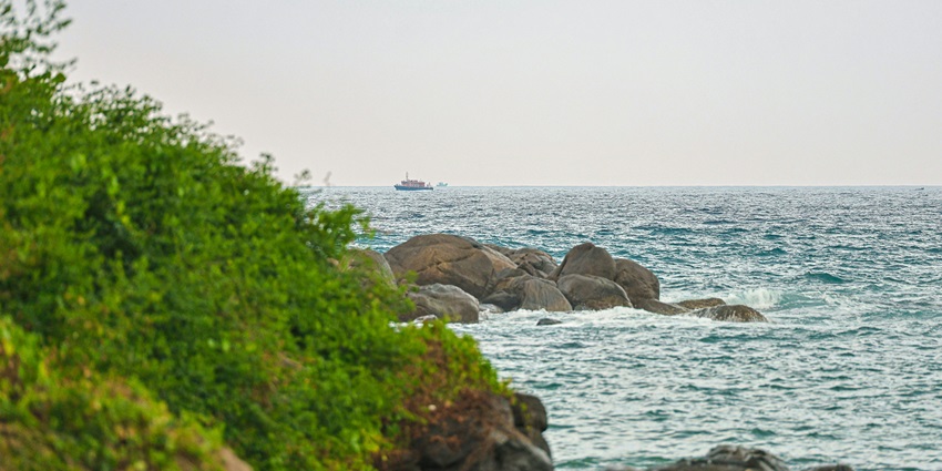 A daytime view of a beach in Kerala with azure waters and lush greenery around it.