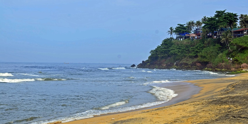 A view of Porkkalam Beach in Kerala with waves crashing on it surrounded by greenery.
