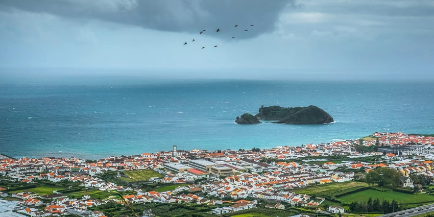 A mesmerising aerial view of a village in Portugal with birds flying in the cloudy skies