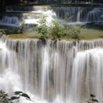 Natural lush greenery besides tea plantations surround these waterfalls, creating a scenic view.