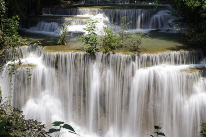 Natural lush greenery besides tea plantations surround these waterfalls, creating a scenic view.