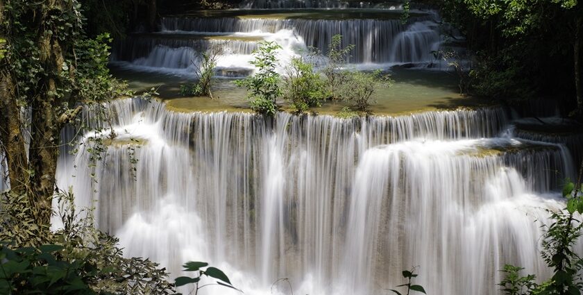 Natural lush greenery besides tea plantations surround these waterfalls, creating a scenic view.