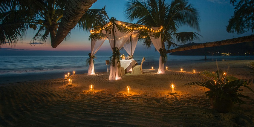 Romantic dinner on the beach during sunset decorated with a tent, candles and lights.
