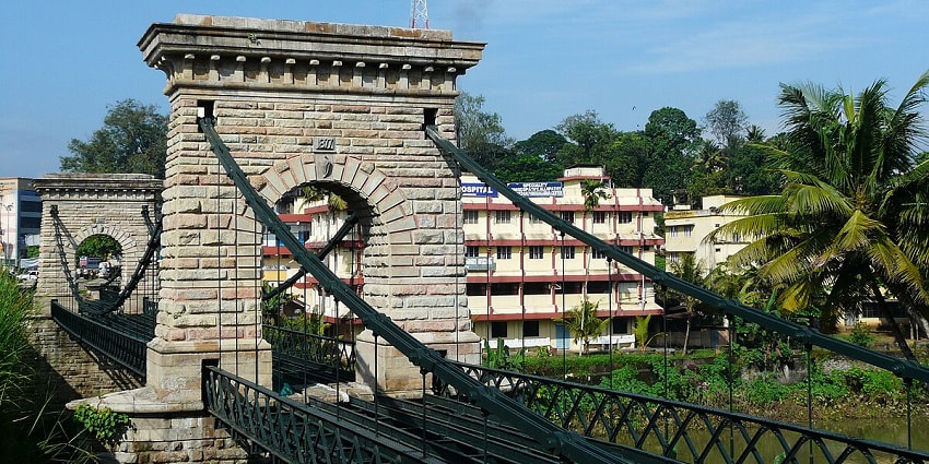A breathtaking view of the suspension bridge in Punalur with tall trees around it.