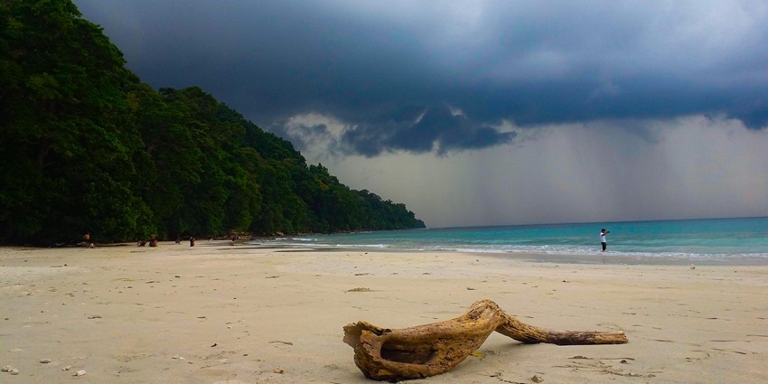 A scenic view of Radhanagar Beach with its golden sands, green forests, and dense clouds