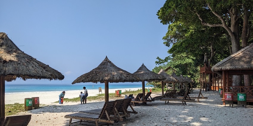 Soft white sands and clear blue waters at the tranquil Radhanagar Beach at sunset.