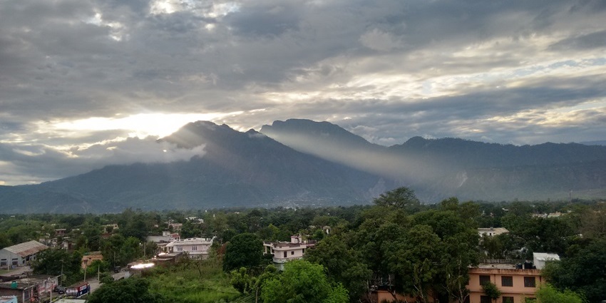 A quaint view of Reasi featuring towering peaks, an idyllic town, and lush greenery.