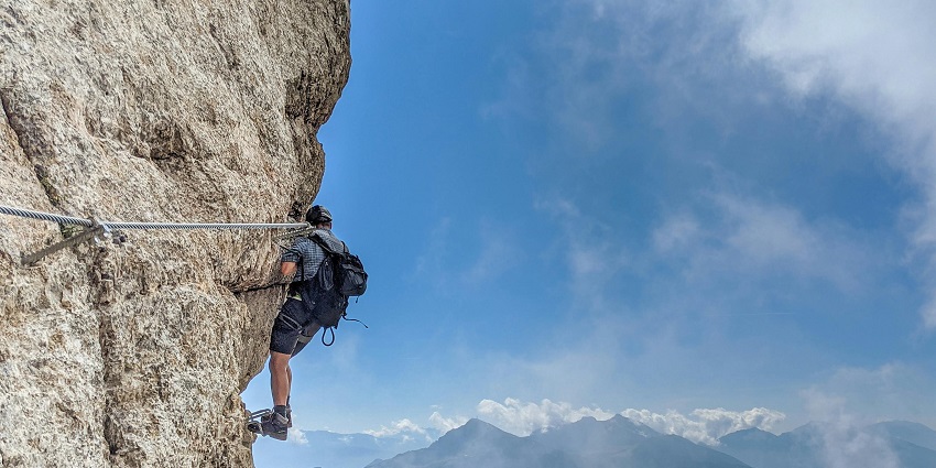 A man clicked while rock climbing with a breathtaking backdrop of clouds & mountain cliffs