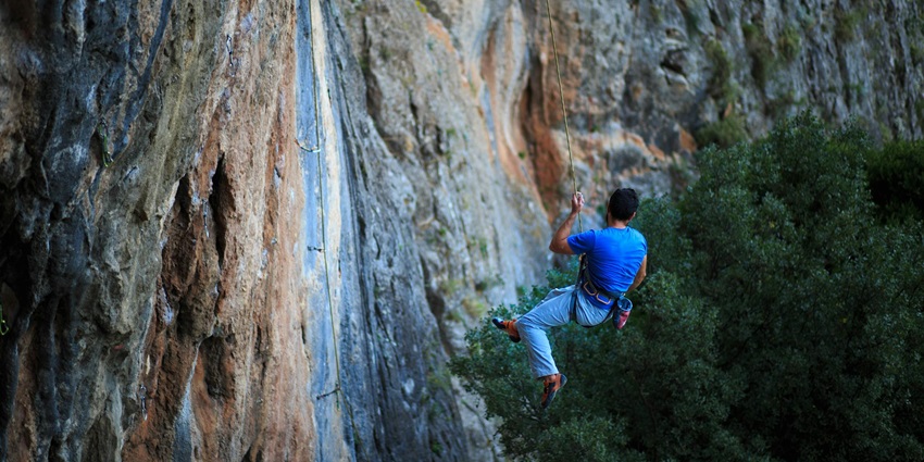 An image of a man in a blue t-shirt and pants attempting to climb a rocky mountain