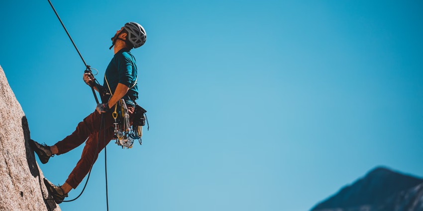 View of a man in a blue shirt and grey helmet attempting to climb a rocky mountain
