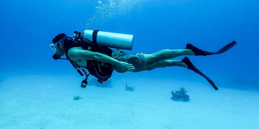 Scuba diver exploring coral reef underwater with sunlight filtering through water