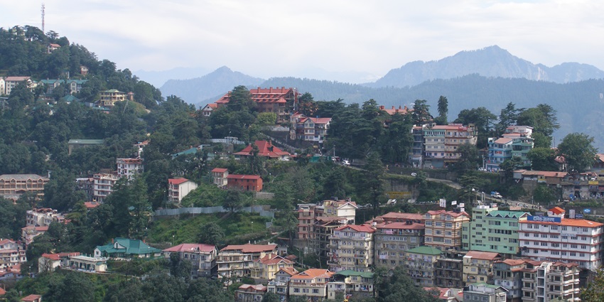 A majestic view of the city of Shimla with residential buildings spread amidst the lush greenery