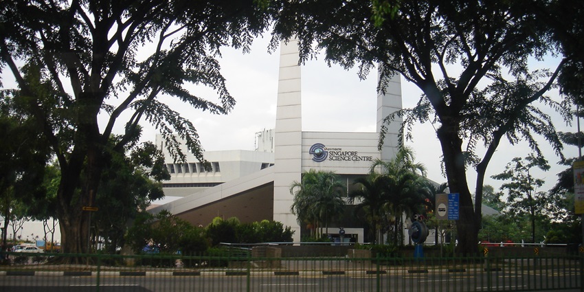 A front view of the Singapore Science Centre covered with lush green trees during the day