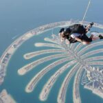 A stunning aerial view of two people skydiving with turquoise waters and an island below.