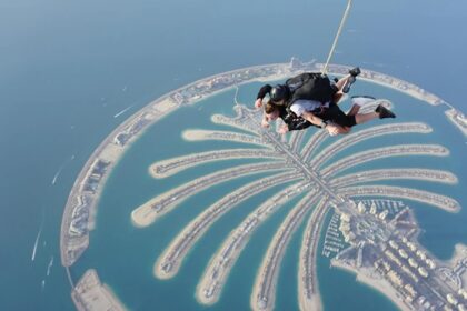 A stunning aerial view of two people skydiving with turquoise waters and an island below.