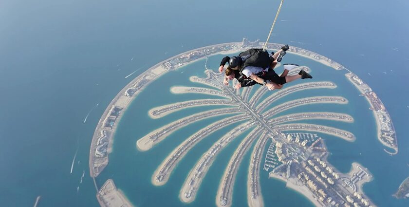 A stunning aerial view of two people skydiving with turquoise waters and an island below.