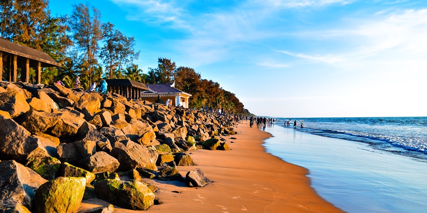 Sunset-lit sandy beach at Snehatheeram with calm waves, palm trees, and family visitors.