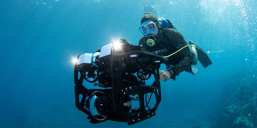 An underwater mesmerising view of a person snorkelling with a big camera in his hands.