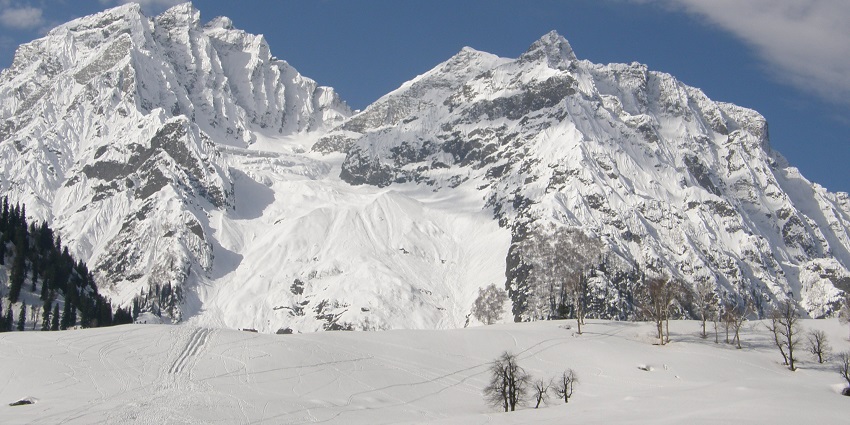 Snow-covered mountains of Sonamarg with pine trees and a clear blue sky in the background