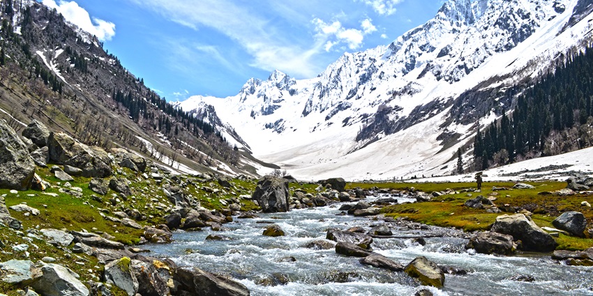 A stunning view of Sonmarg with snow-capped peaks in the background and a stream of water.