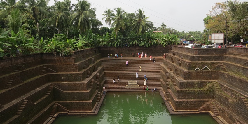 A picture of a downward staircase along pine trees, leading to a sacred pond at a temple