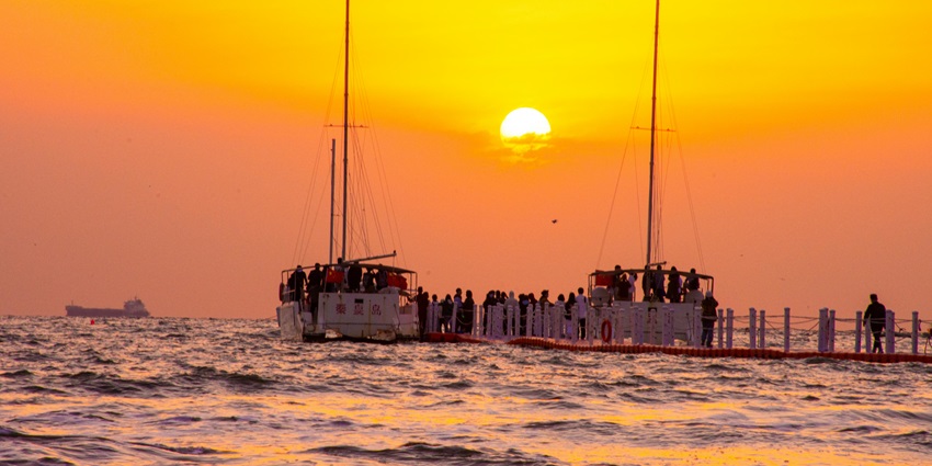 Sailboat gliding on calm sea beneath a vibrant pink and purple sunset sky