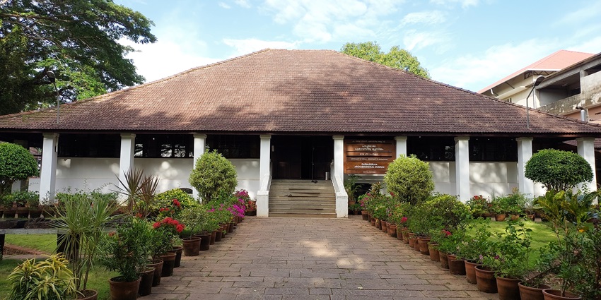 A frontal view of the Pazhassiraja Archaeological Museum, surrounded by lush green gardens