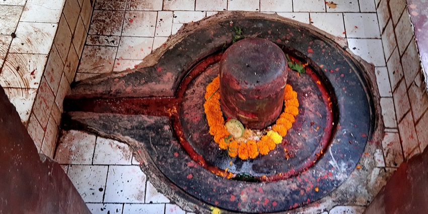 A temple with Shiv Ling and intricate architectural details surrounded by lush greenery.