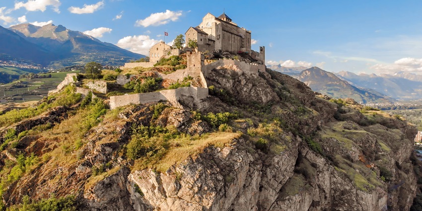 A view of the scenic Valère castle perched up on a mountain, surrounded by lush greenery
