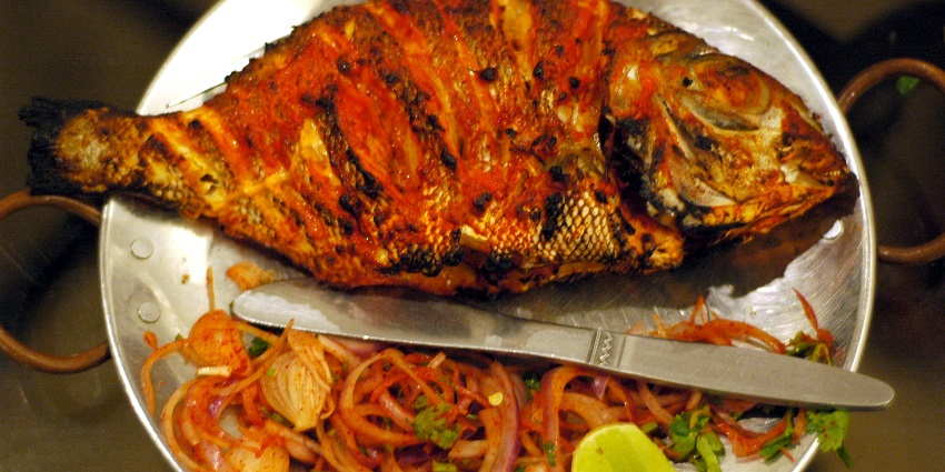 Image of tandoor fish, perfectly grilled with spices, served with a side of fresh onions.