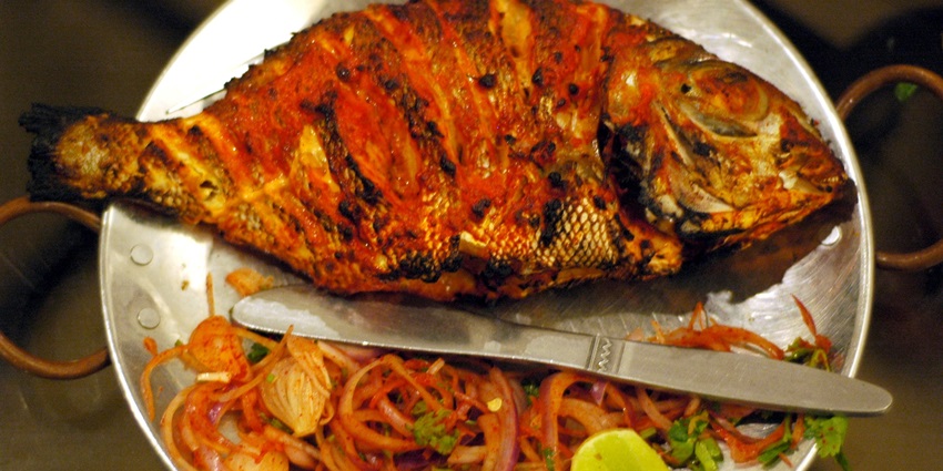 Plate of grilled tandoori fish, garnished with aromatic spices and served with lemon