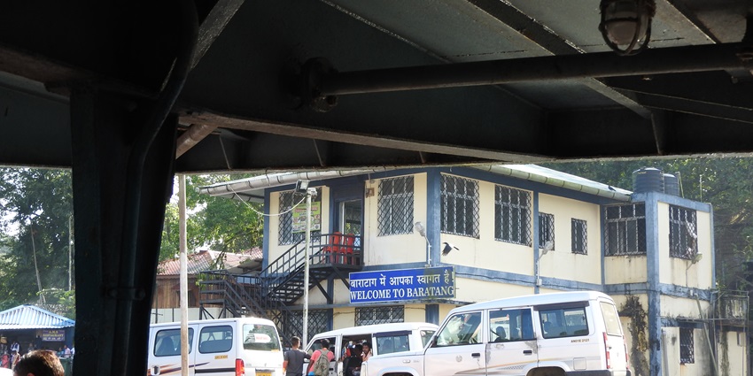 View of taxis on Baratang Island with people waiting in a queue with a blue board behind.