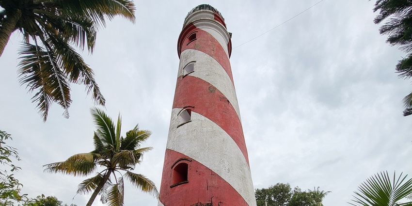 A picture of a light house at a sea shore in Kerala, surrounded with pine trees
