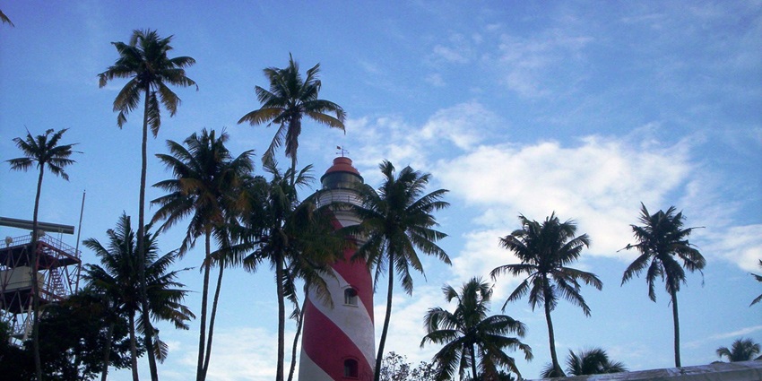 Scenic view of Thangassery Light House with palm trees in front & cloudy skies at the back