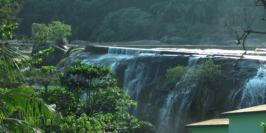 Wide cascading waterfall flowing over a rocky ledge, surrounded by lush greenery.