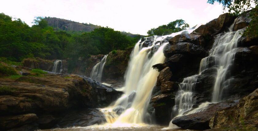 Scenic view of descending Thoovanam Waterfall amidst the lush greenery and hills