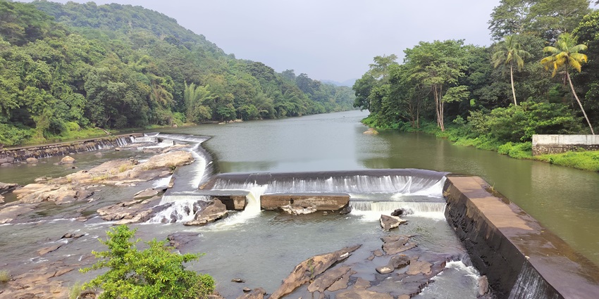 View of the Thumboormuzhy Dam with lush green forest and clear skies in the background